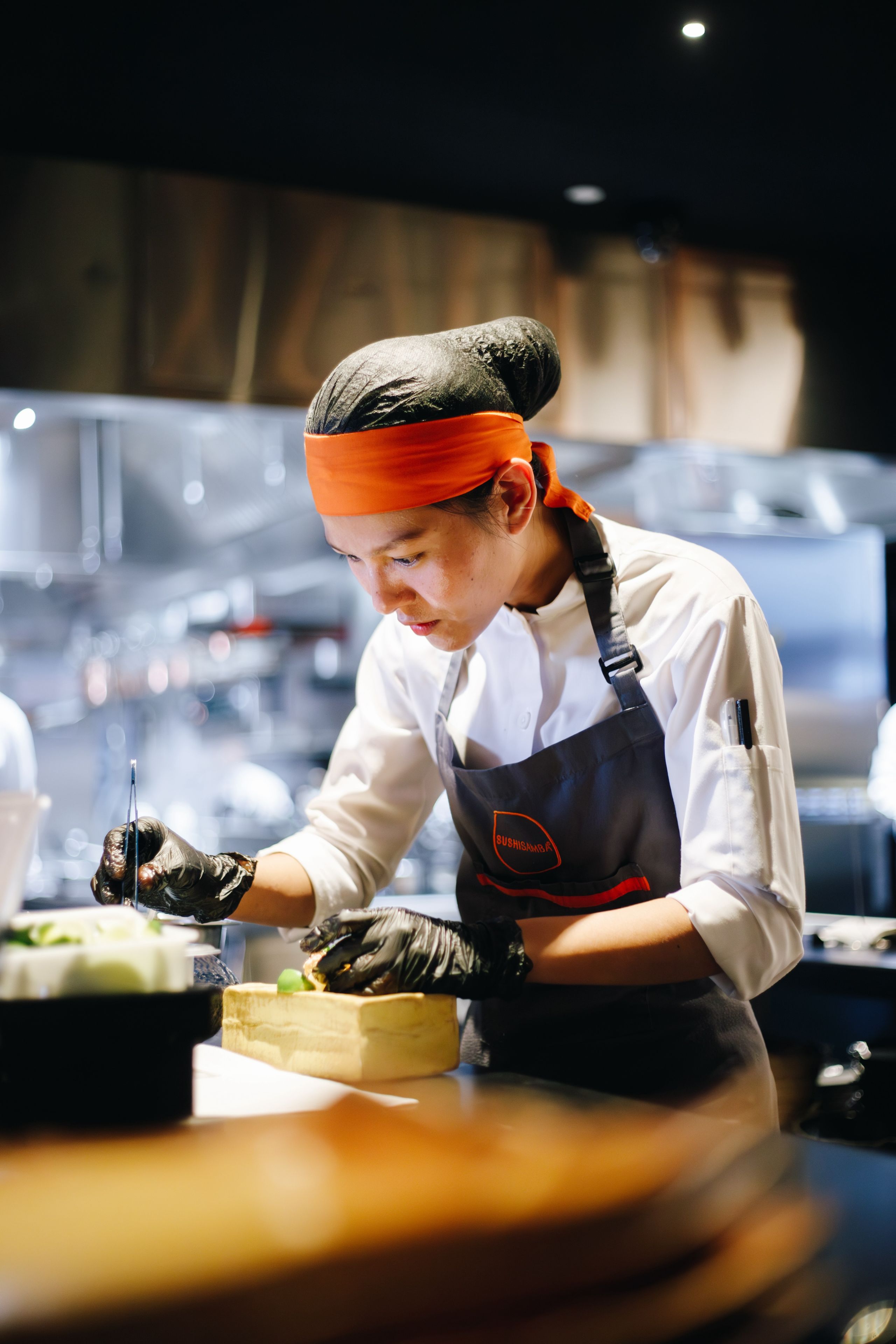 SUSHISAMBA female chef working in the kitchen, putting finishing touches on a dish